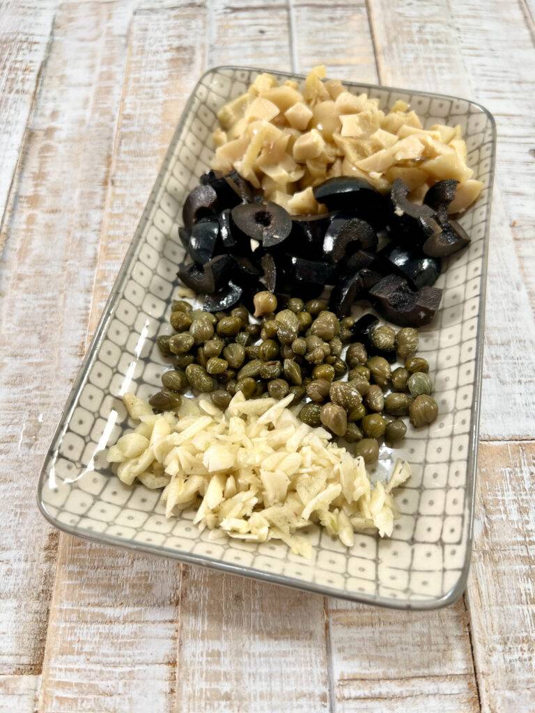 Prepared ingredients: Minced garlic, capers, and diced olives on plate