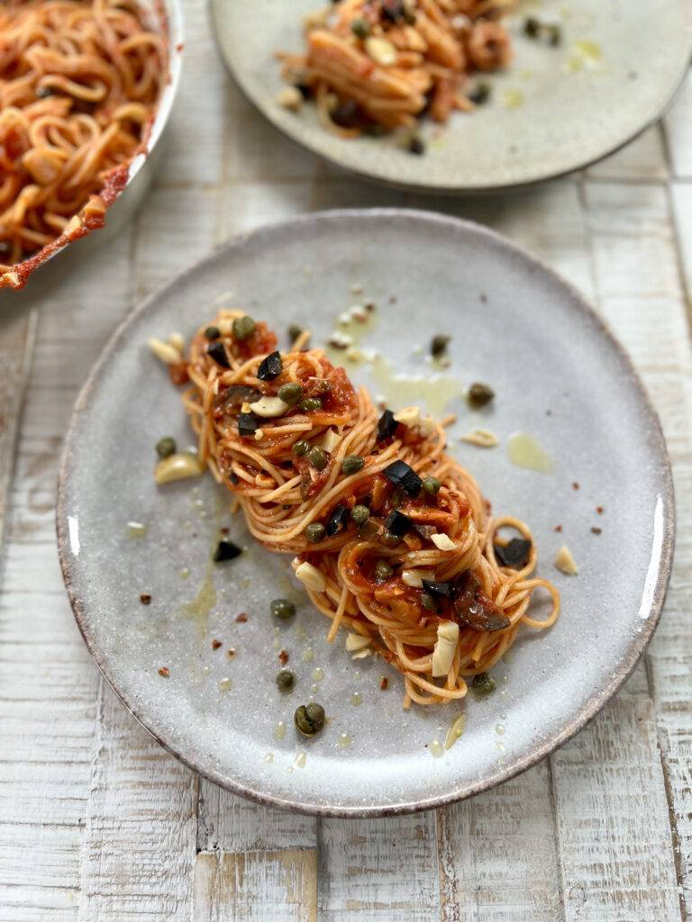Spaghetti alla puttanesca plated, garnished with olives and capers