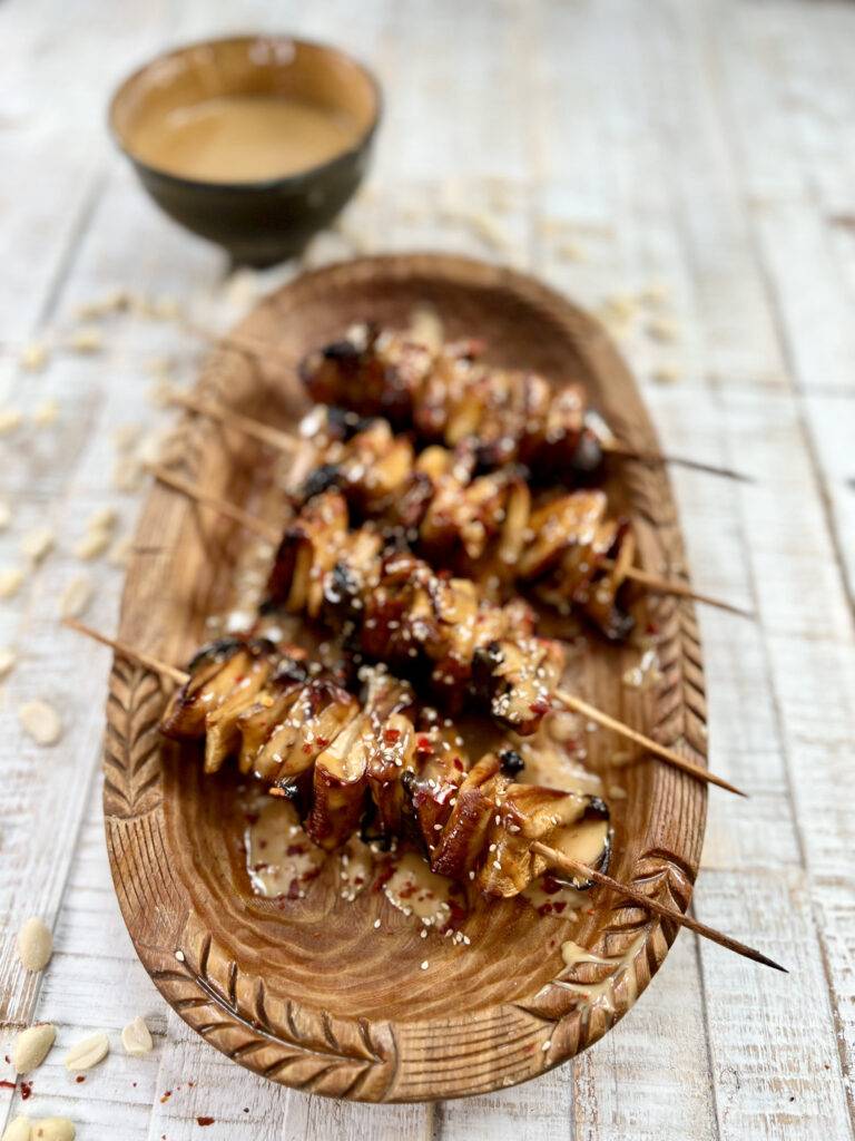 Vegan mushroom skewers topped and plated with peanut sauce on wooden plate
