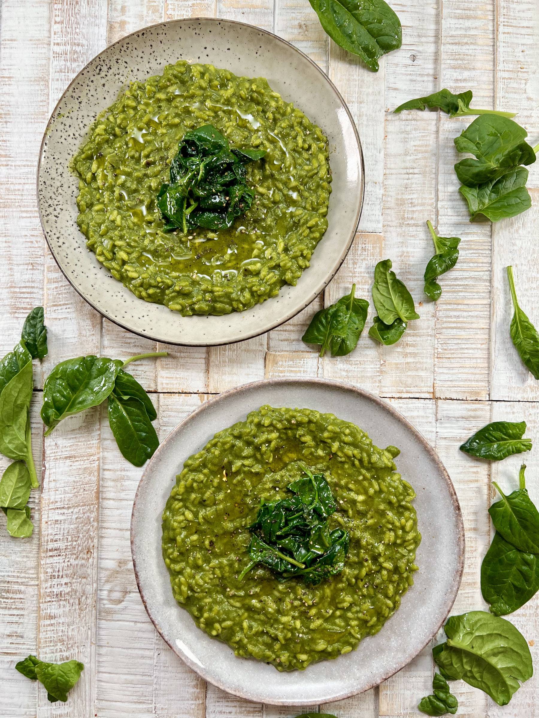 Vibrant green spinach risotto plated on grey plates with spinach leaves as garnish around them. Bird eye angle.