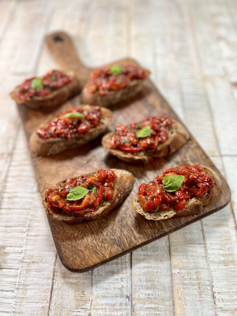 five sweet pepper crostini plated on a wooden board