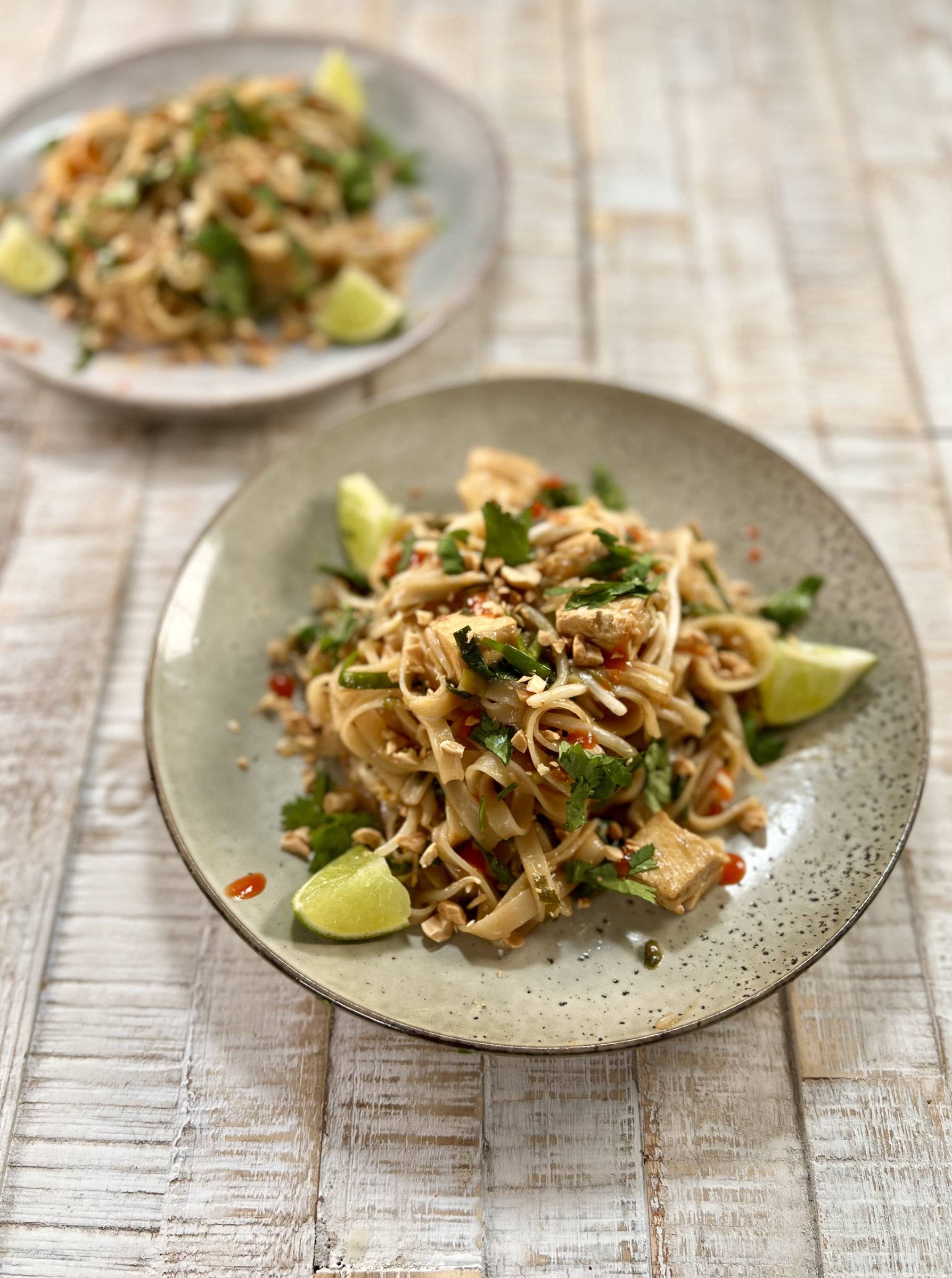 Vegan Pad Thai Plated with lime wedges and sriracha on a grey plate on wooden surface.