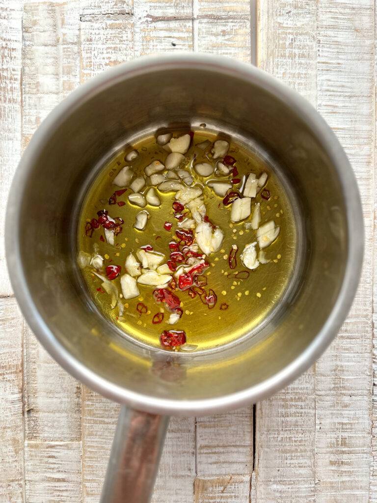 Crushed garlic cloves and chilli infusing in olive oil in a stainless steel pot