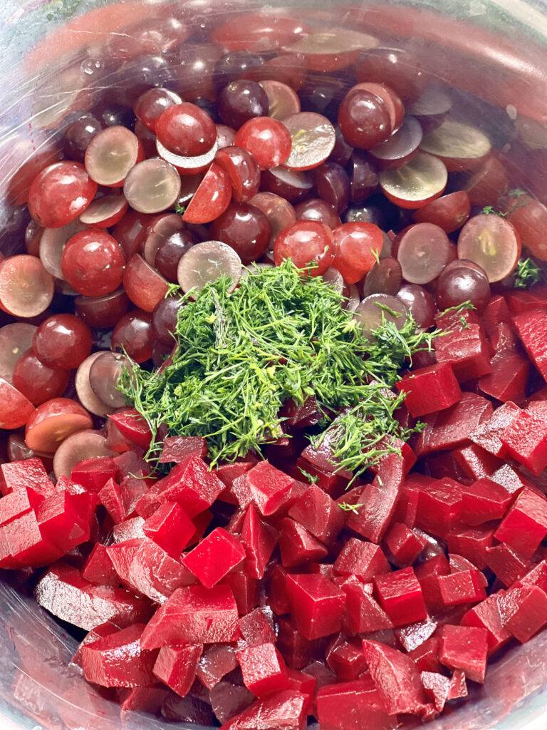 Diced beets. sliced grapes and chopped dill in stainless steel bowl