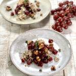 Two plates of beautifully garnished red beet salad, with grapes next to them.