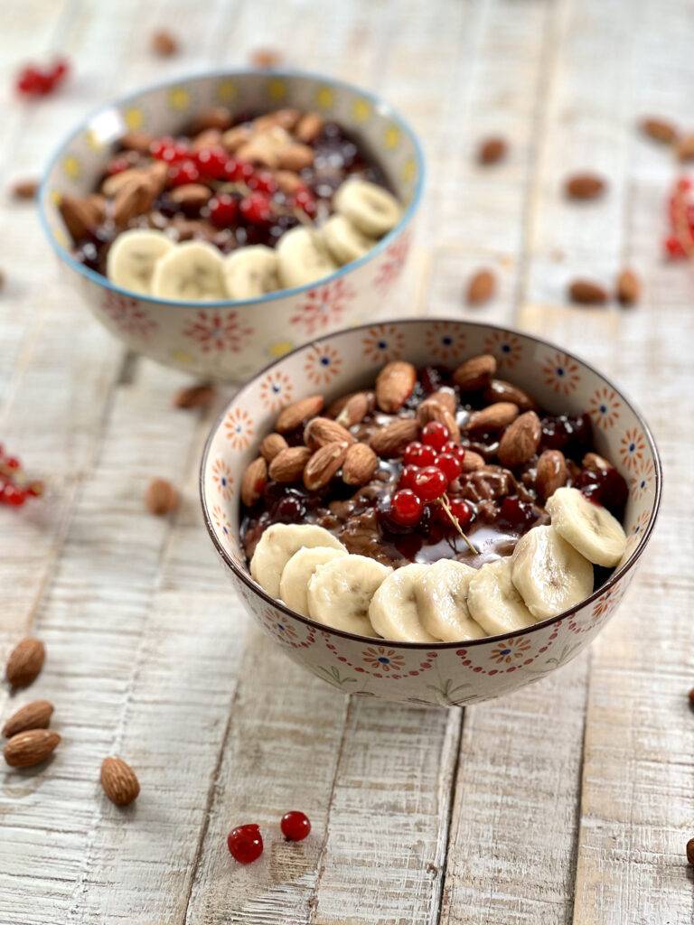 Plated sweet rice porridge in two bowls, garnished with banana slices, red currant, and almonds
