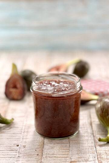 Fig chutney in jar, with figs around it on wooden surface