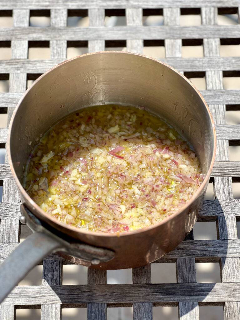 The finely diced onion melting away in oilve oil in a copper pot, building the base of the tomato sauce
