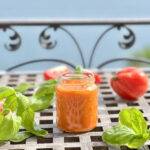 A jar of homemade tomato sauce in front of a beautiful lake view, decorated with basil and fresh tomatoes