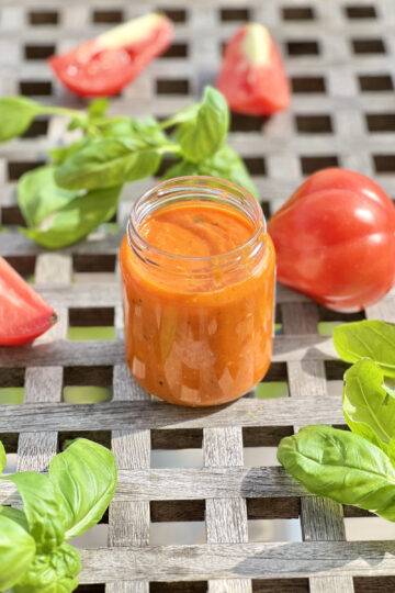 Jar of homemade tomato sauce on a wooden table, garnished with basil and fresh tomatoes
