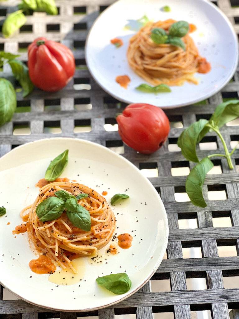 Two plates of pasta al pomodoro with homemade tomato sauce, beautifully garnished with fresh basil