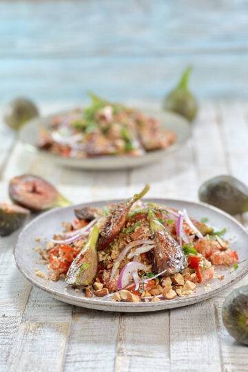 A beautifully garnished, colorful fig couscous salad with almonds on grey plates