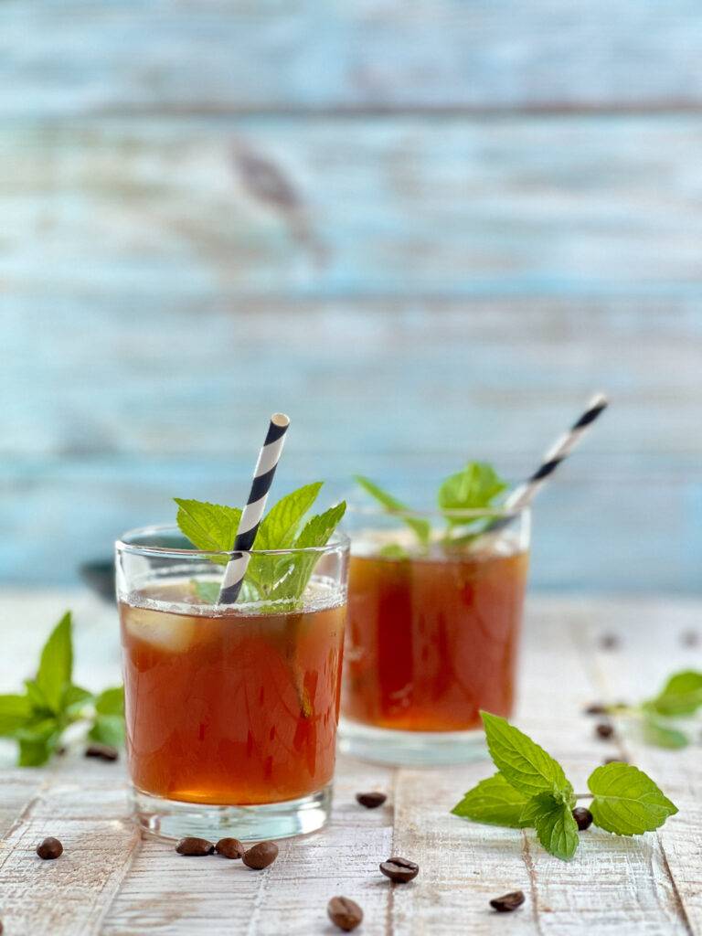 Two glasses of beautifully garnished Espresso tonic in front of a blue wooden background