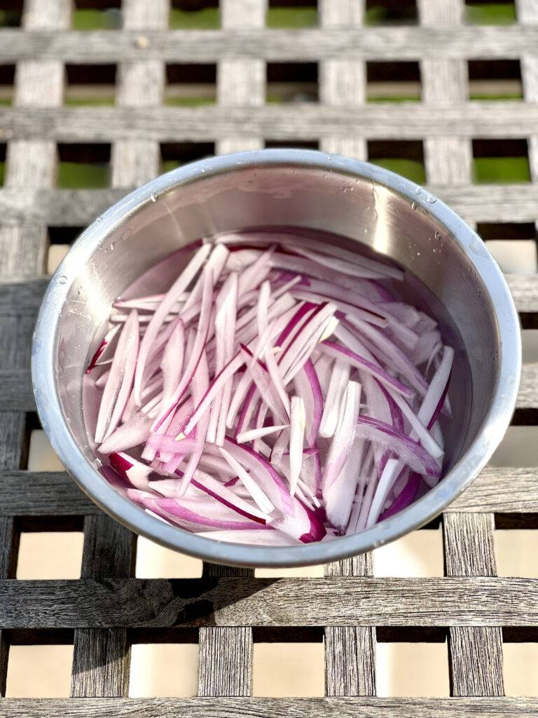 Red onion strips in a cold water bath in a stainless steel bowl