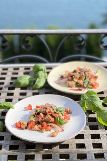 Two plates of Panzanella plated with basil in front of a beautiful lake view