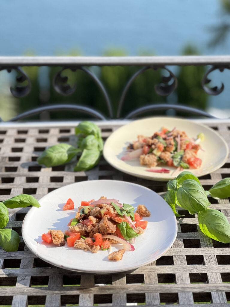 Two plates of Panzanella plated with basil in front of a beautiful lake view