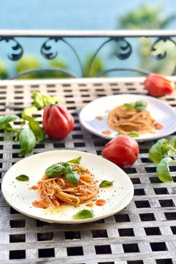 Two plates of pasta al Pomodoro on a wooden table, beautifully garnished in front of a lake view