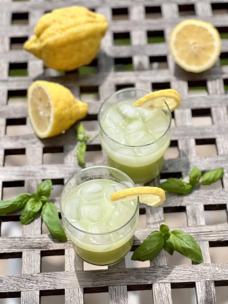 Two glasses of basil lemonade and a slided lemon garnished with fresh basil