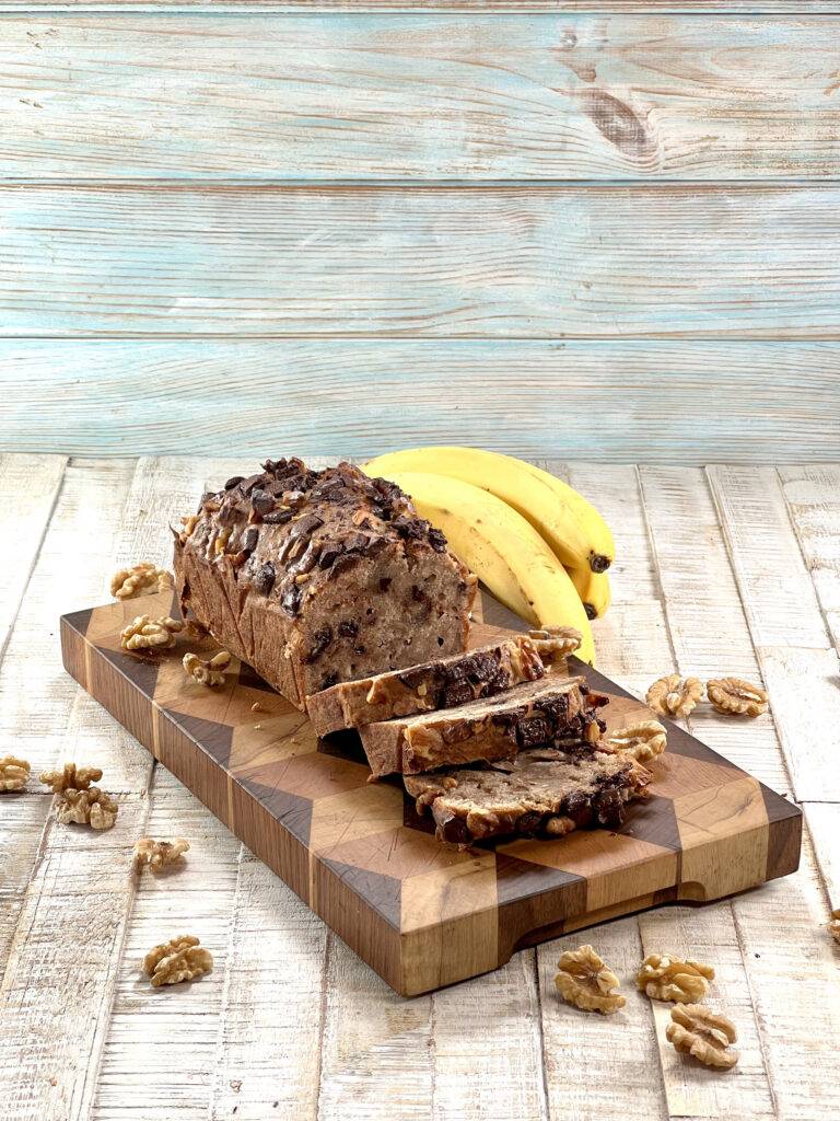 Sliced banana bread with walnuts tossed around it and bananas in the background