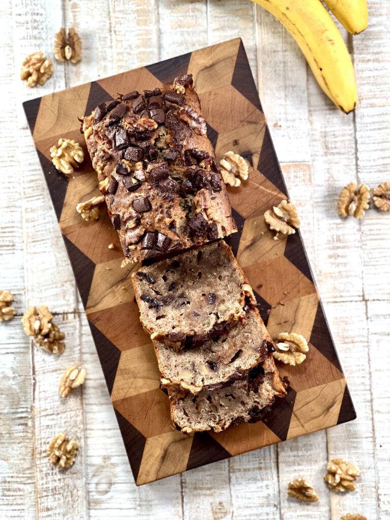 Top angle of sliced banana bread on a wooden board decorated with walnuts and bananas