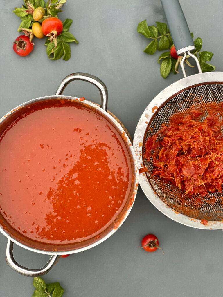 A pot with strained rose hip jam, and a sieve with the remaining skins 