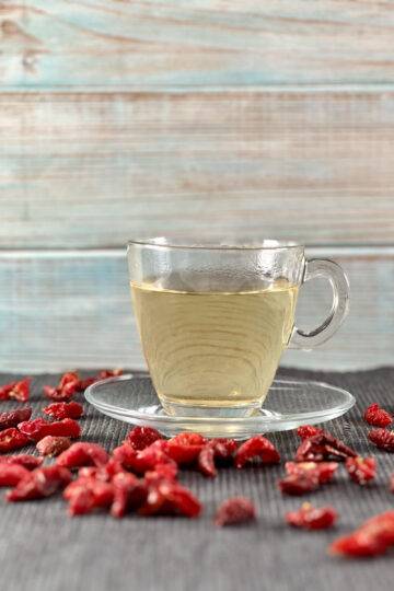 A cup of rose hip tea with dried rose hips around it
