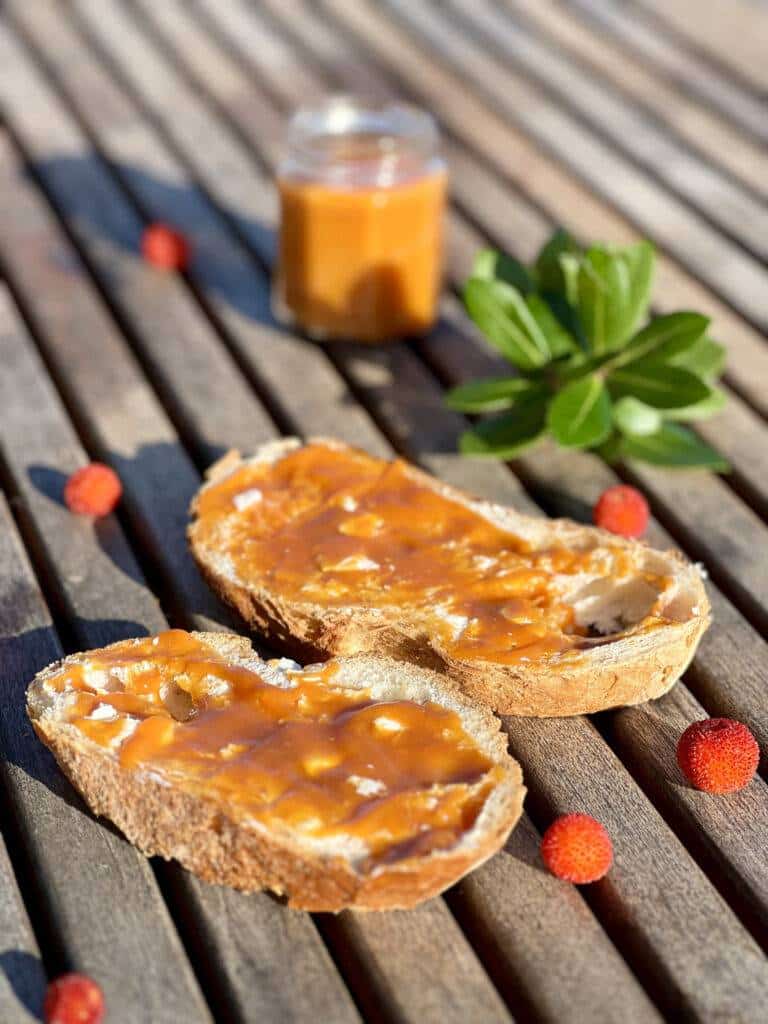 Two slices of bread with strawberry tree jam on a wooden jam