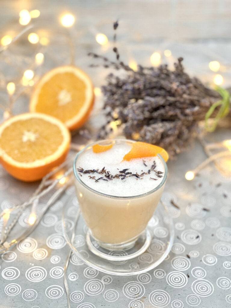 Beautifully decorated lavender milk tea with a sliced orange and dried lavender in the background