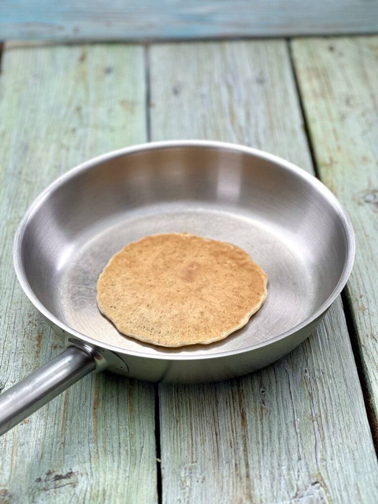 A vegan banana pancake in a stainless steel pan