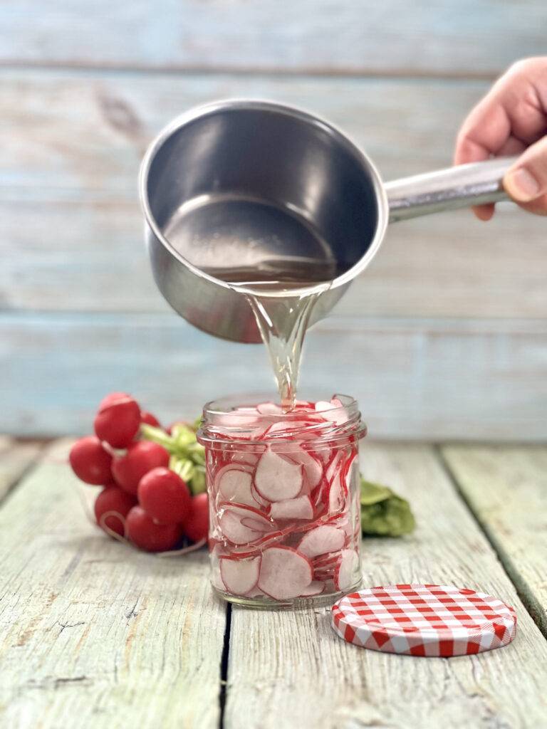 Jar with sliced radish with hot brine being poured in to it