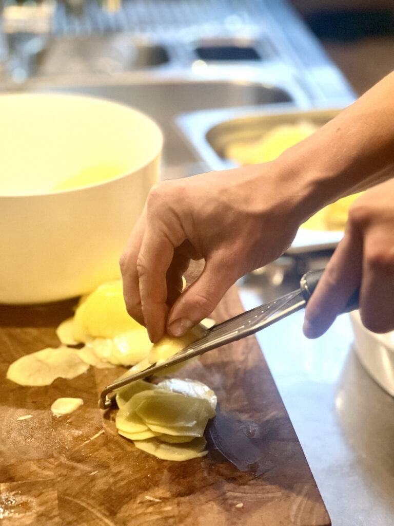 Slicing potatoes with a mandoline slicer on a wooden cutting board