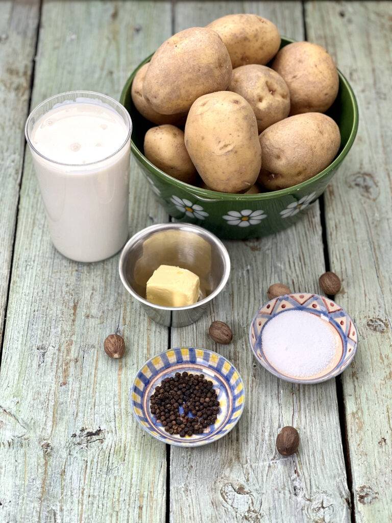 Ingredients for vegan potatoes au gratin in bowls (potatoes, soy cream, vegan butter substitute, salt, pepper and nutmeg)