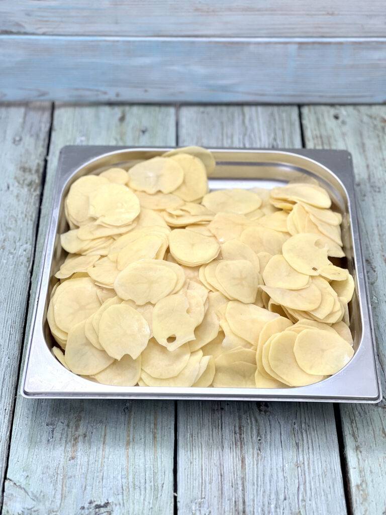 Thinly sliced potatoes in a stainless steel kitchen tray