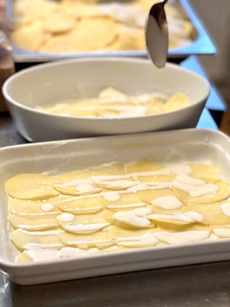 Layering potatoes and soy cream in two ceramic casseroles