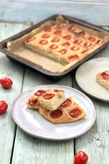 Two slices of focaccia plated, garnished with cherry tomatoes