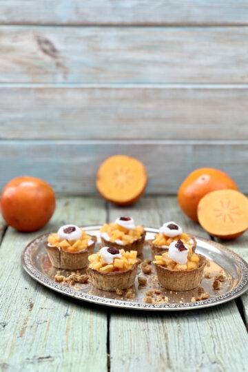 Beautiful persimmon tarts on a silver tray with two sliced persimmons around them