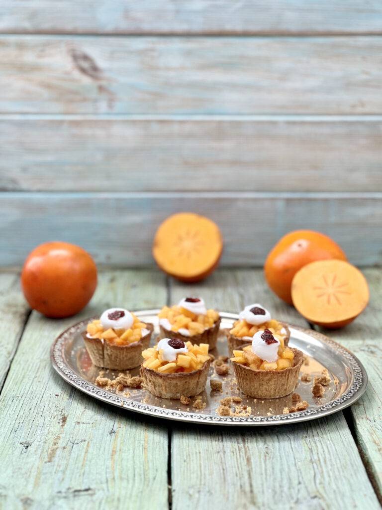 Beautiful persimmon tarts on a silver tray with two sliced persimmons around them
