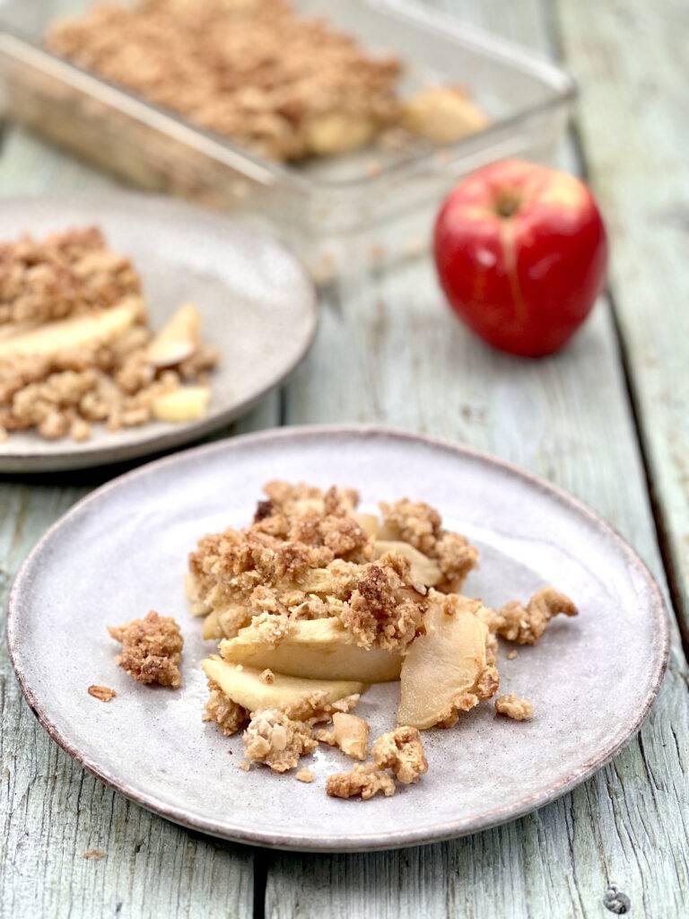 Two plates of apple crisps with a apple in the background