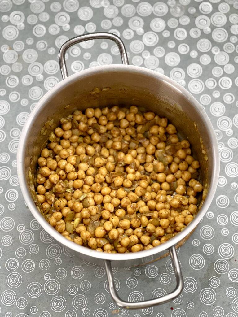 Spice coated, sautéed onions and chickpeas in a stainless steel pot