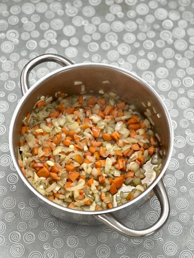 Diced vegetables sautéing in a stainless steel pot