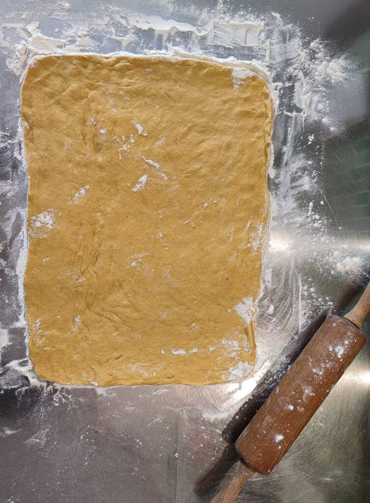 Roll out the yeast dough on a stainless steel work surface with flour. A rolling pin is attached.