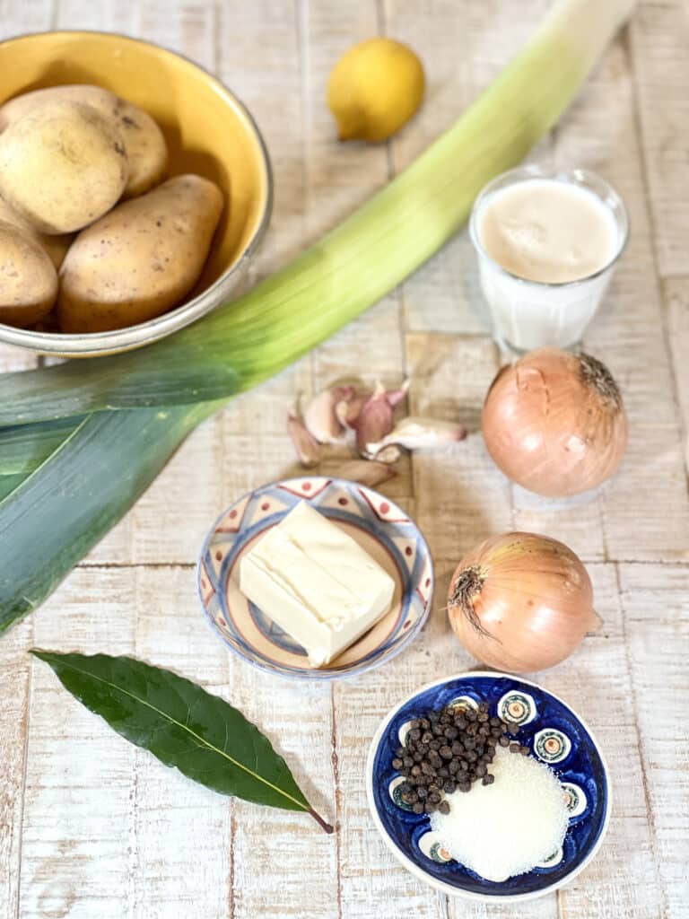 Ingredients for making vegan vichyssoise on wooden table (leek, potatoes, vegan butter substitute, garlic, vegan cream substiute, lemon, garlic. salt and pepper, laurel leaf)