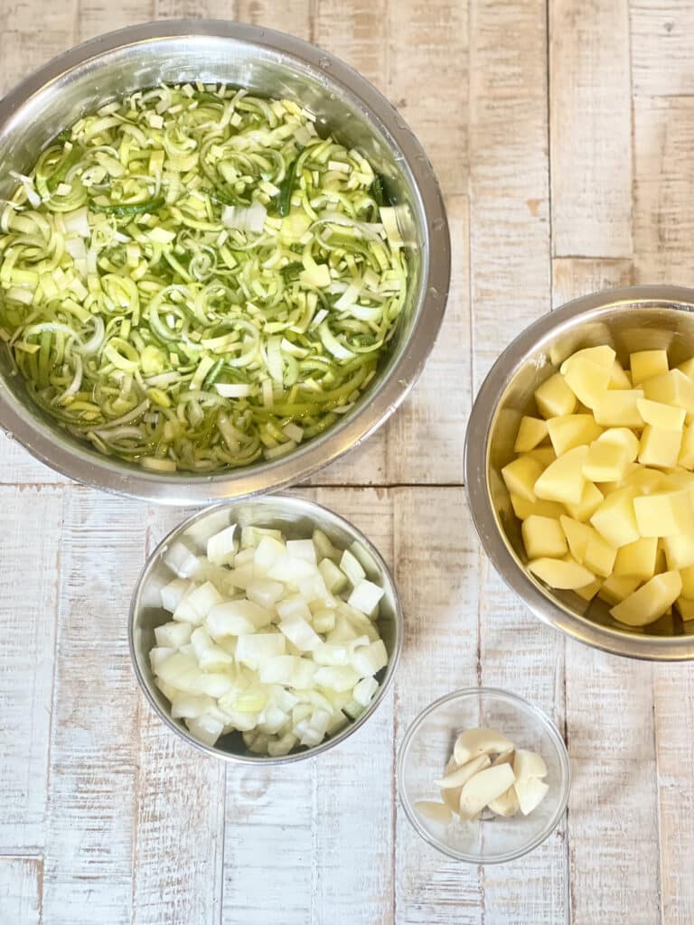 Thinly sliced leek, diced potatoes, diced onions, and minced garlic in little bowls