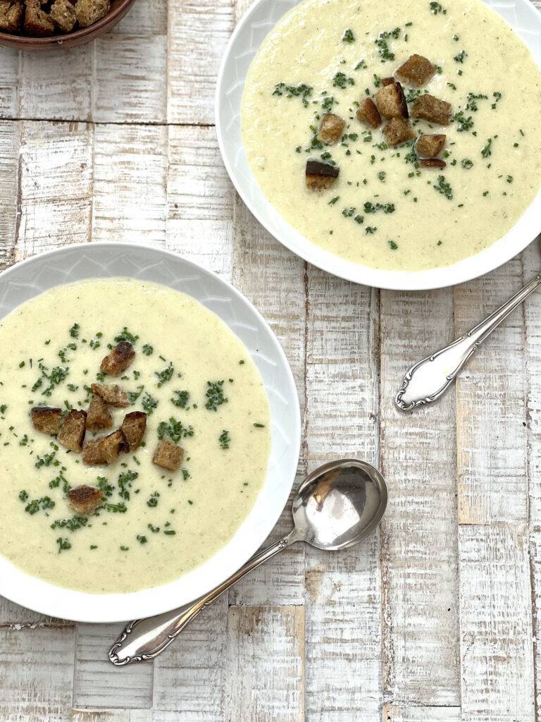 Two white plates filled with smooth vegan vichyssoise, garnished with chives and croutons.