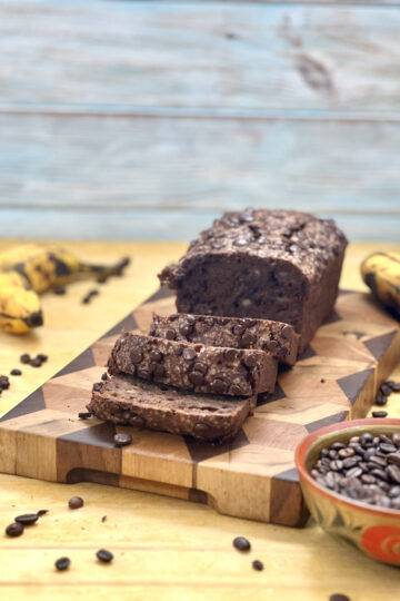 A loaf of coffee banana bread sliced and served on a wooden plate, garnished with coffee beans