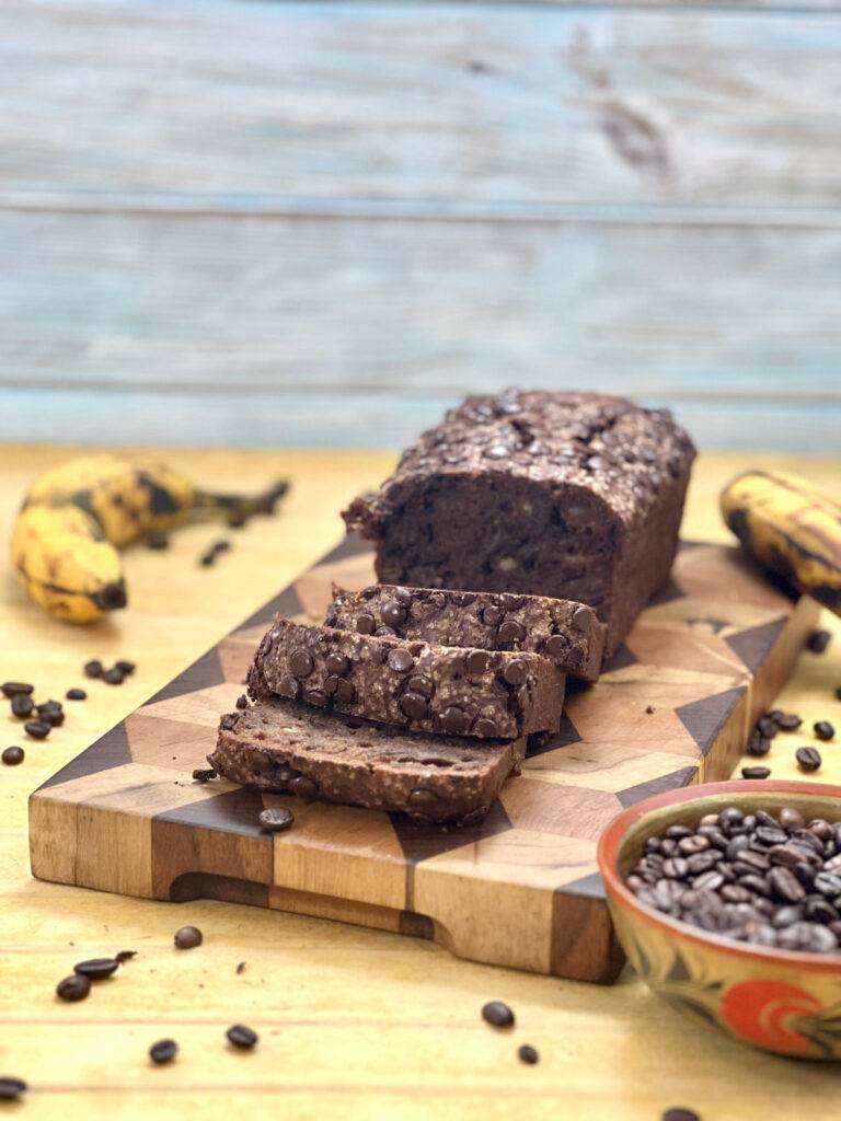 A loaf of coffee banana bread sliced and served on a wooden plate, garnished with coffee beans