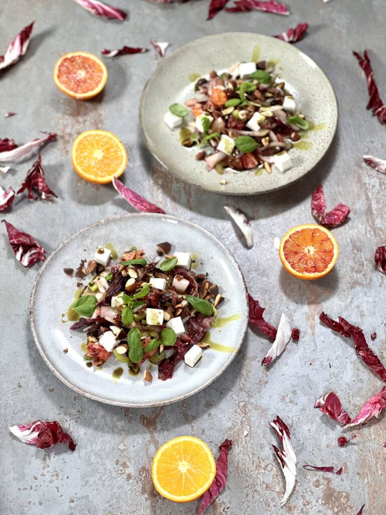 Two plate of radicchio salad on a dark stone underground with sliced blood oranges and pieces of radiccho around them