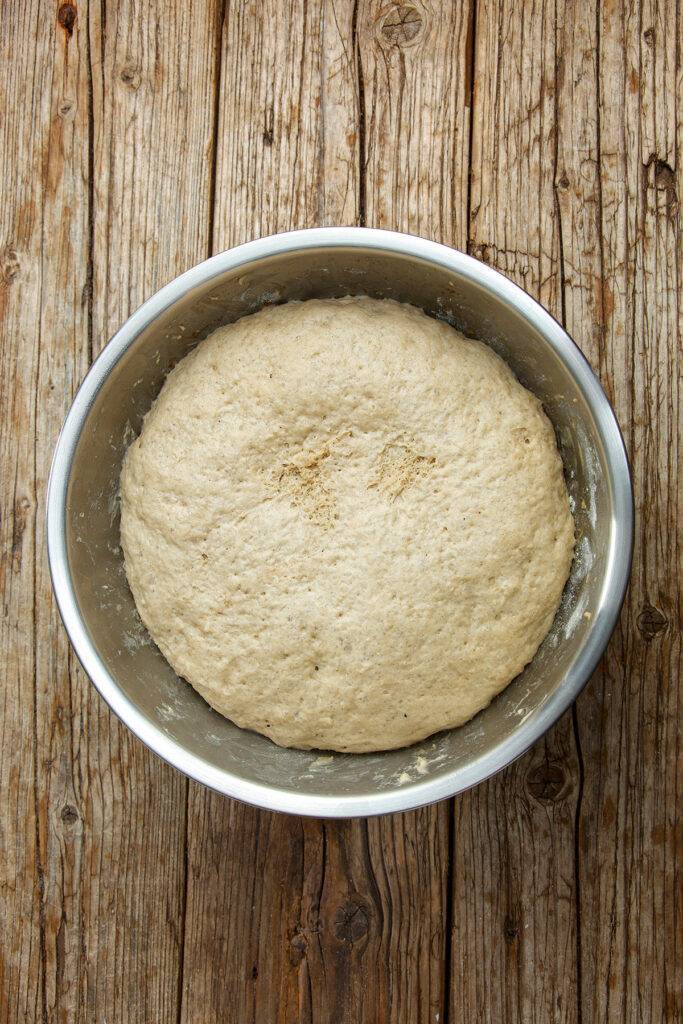The risen yeast dough lies in a stainless steel bowl. The base is made of wooden planks.