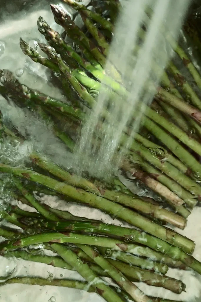 The asparagus is washed in the sink with a jet of water.
