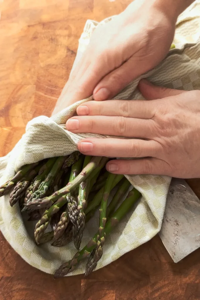 On a wooden table, the asparagus is wrapped in a towel and held by the hands.